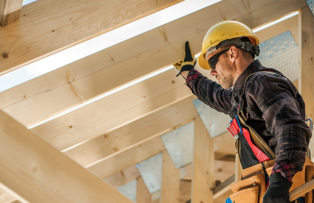 Timmerman met veiligheidshelm bij een houten dakconstructie